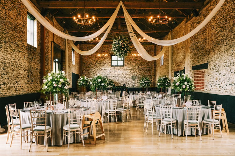 interior of a barn wedding venue set up for a Christmas wedding reception with tall green and white tablecentres.