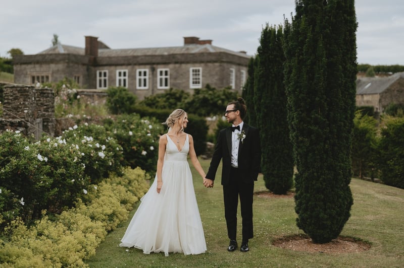 a bride and groom holding hands and smiling at each other outside a Georgian manor house wedding venue.