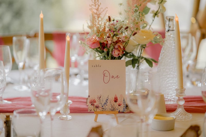 close up of a wedding breakfast table featuring candles, flowers and a small easel with a floral printed card with table number.