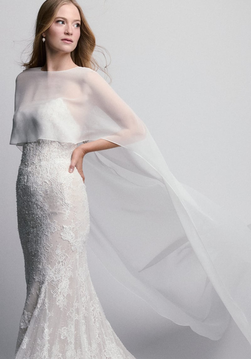a model wears a lace fit-and-flare wedding dress with chiffon cape.
