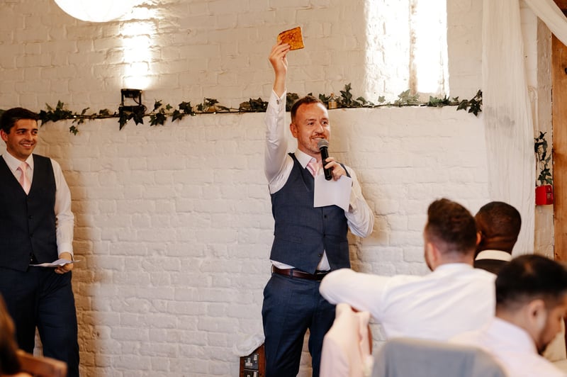 a best man holds up a piece of toast as he gives his best man speech.
