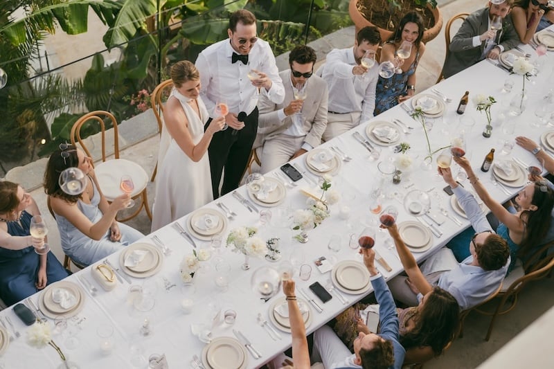 Hochzeitspaar stößt mit Gästen an einer langen Hochzeitstafel an