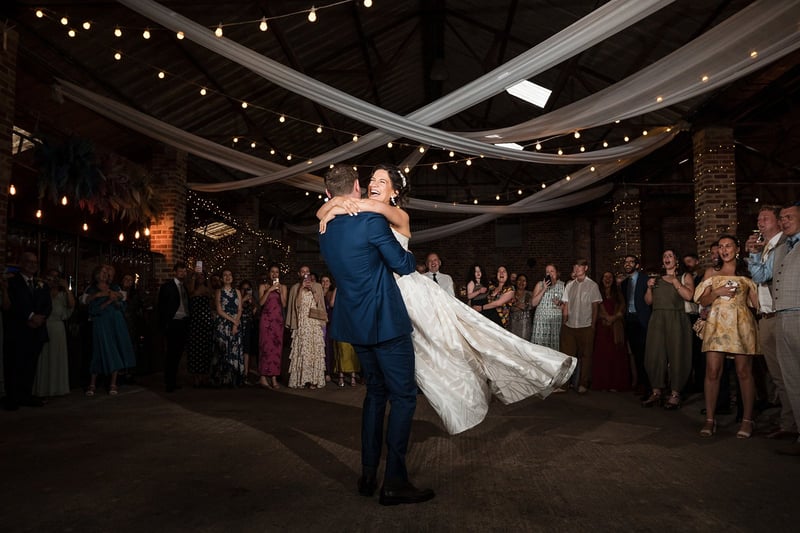 a bride smiles as her groom lifts her during their wedding first dance.