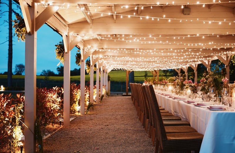 a covered marquee wedding reception with fairy lights on the ceiling as the sun sets.