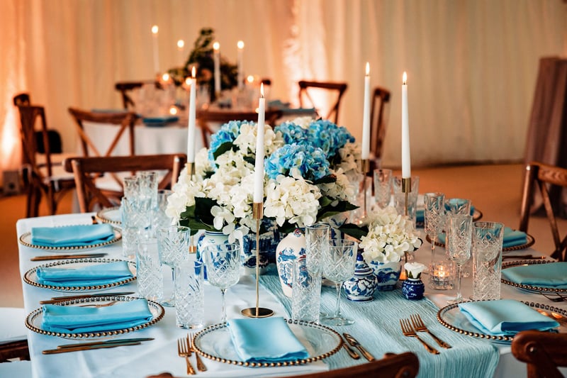 a wedding table with blue and white decor, including white and blue hydrangea arrangements, taper candles and copper cutlery.