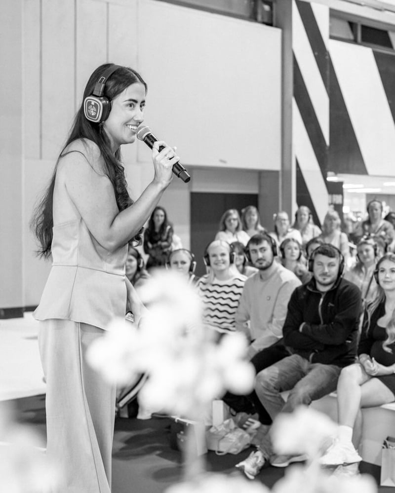 black and white image of a woman holding a microphone as she addresses a crowd on stage at the national wedding show.