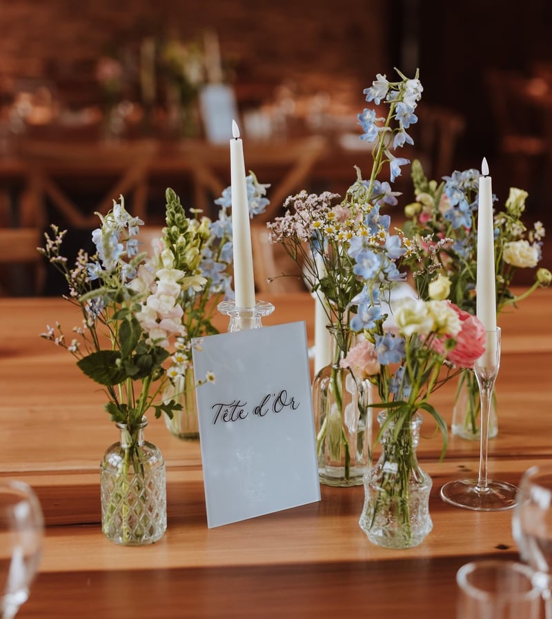 a collection of small glass bud vases filled with pastel coloured wildflowers interspersed with taper candles.