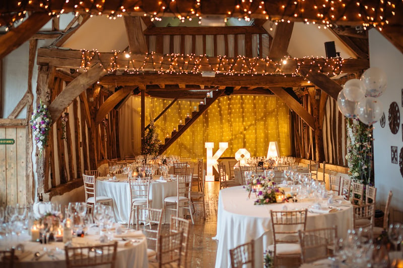 interior of a barn wedding venue set up for a wedding breakfast with round tables and light-up letters.