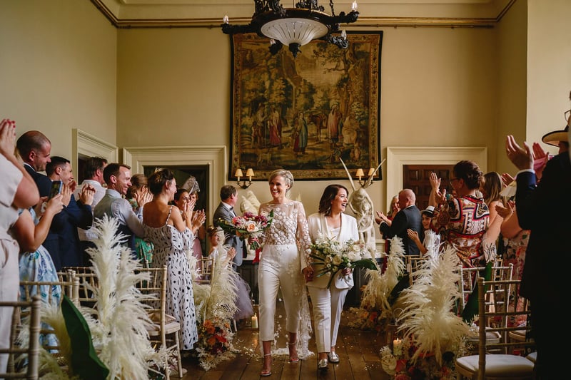 a lesbian couple walk down the aisle happily after their ceremony as guests clap.