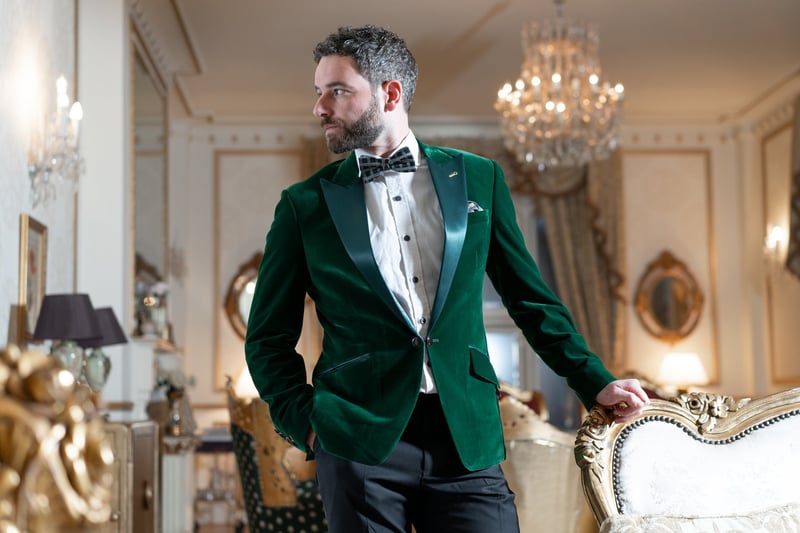 a male wedding guest in a stately home venue wears a green velvet tux jacket with black trousers and white shirt.