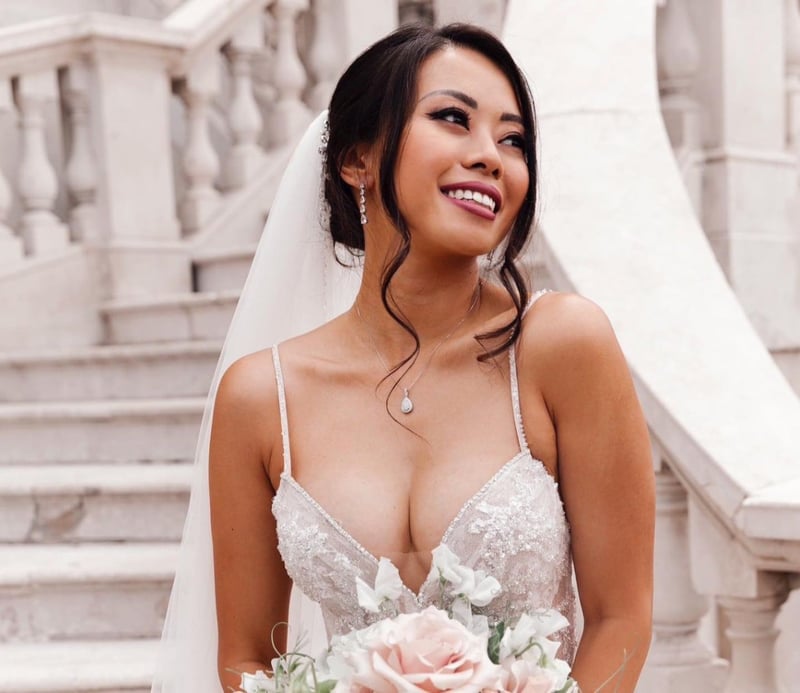 an east asian bride with full glam makeup posing in her wedding dress and veil.