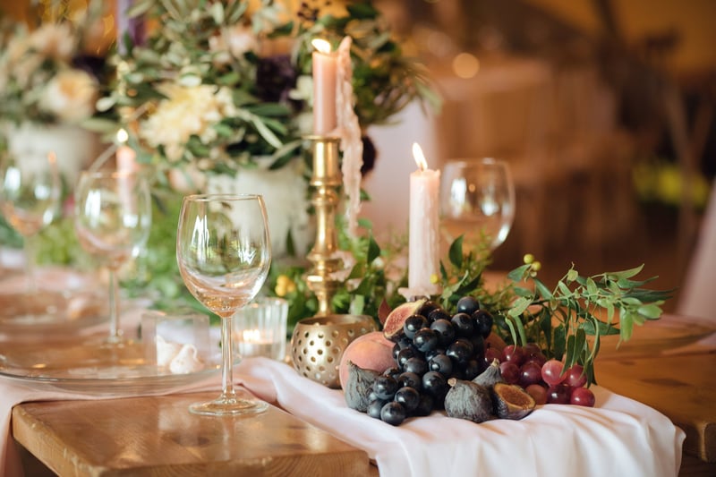 close up of a table with a foliage runner, fruit and candlesticks in gold holders.