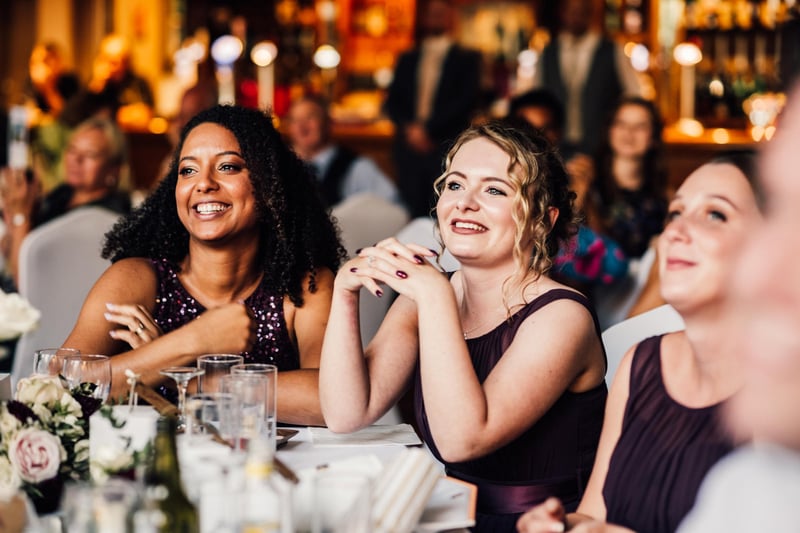 a group of female guests at a table smile as they listen to the best man speech.