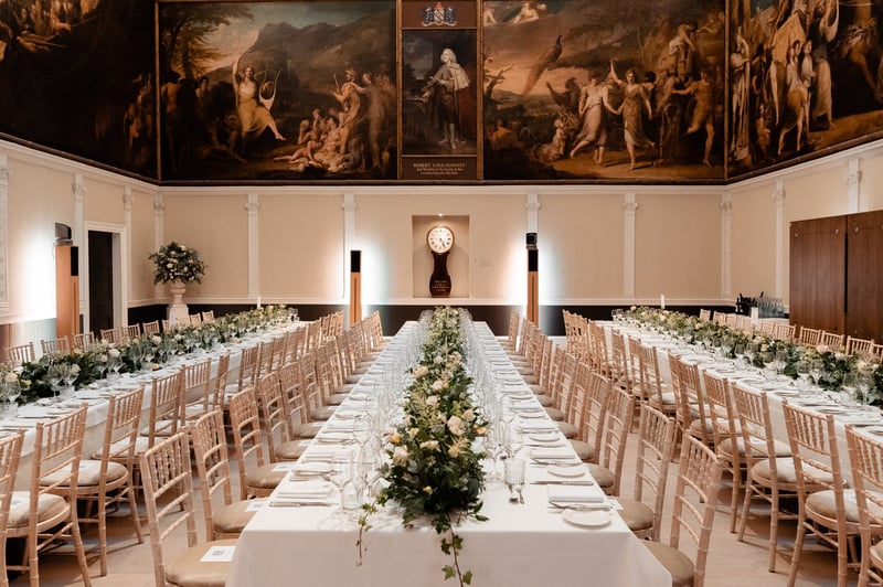 interior of a London wedding venue with period murals on the walls and long tables set up for a Christmas wedding dinner.