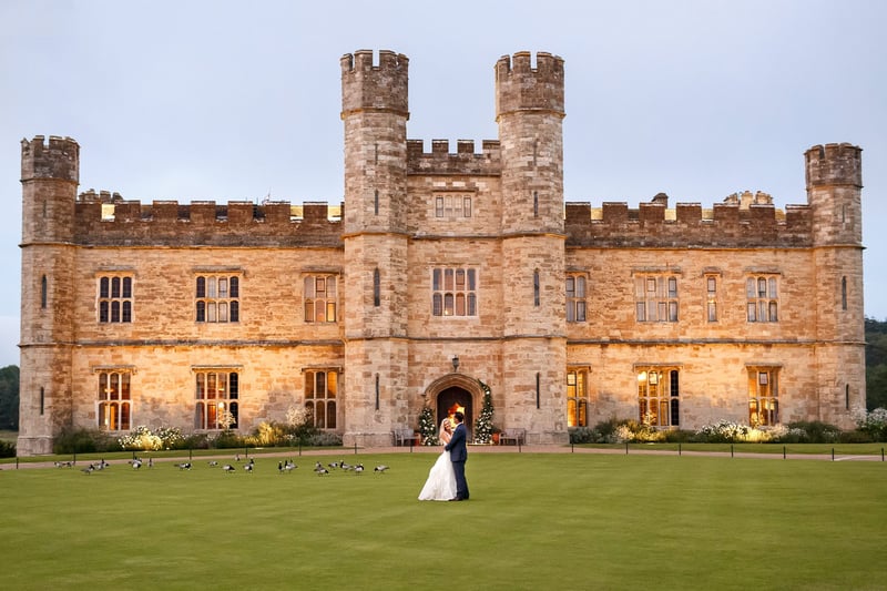 a bride and groom stand in front of a grand castle wedding venue.