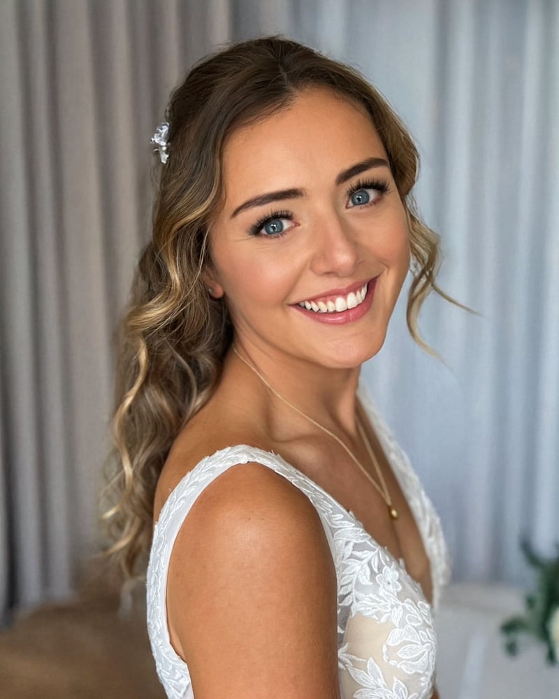 a bride with natural wedding makeup and wavy blonde-brown hair smiles at the camera.