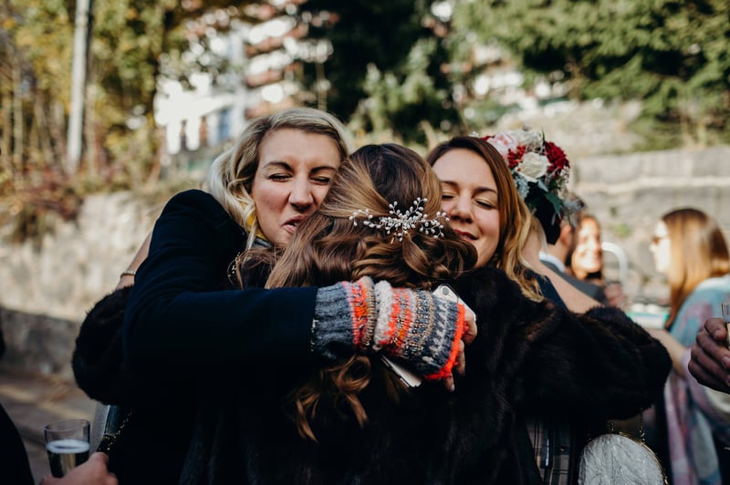 two female guests wearing winter attire and gloves hug the bride at her wedding.