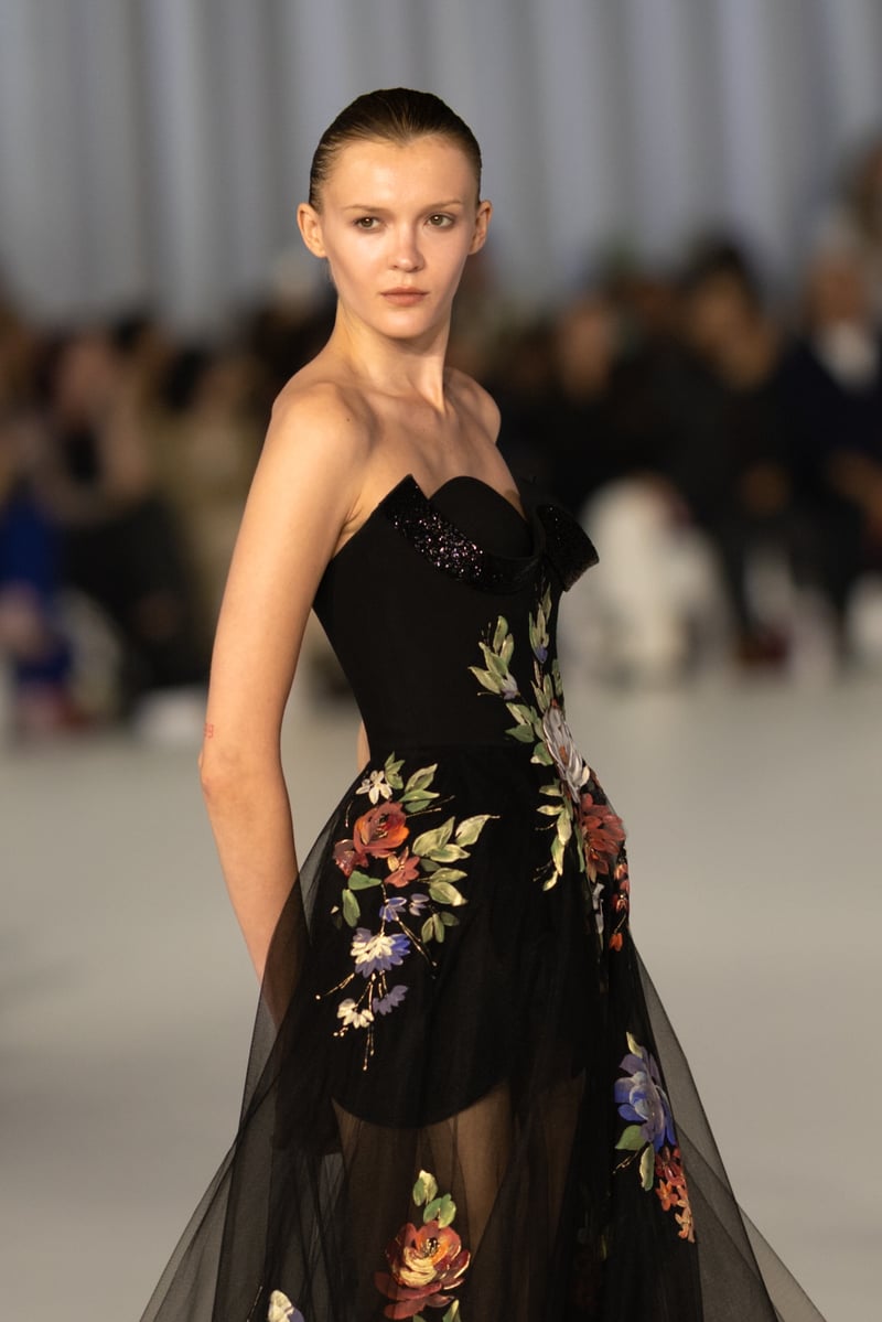 a model on a runway wearing a black wedding dress with russet and green floral embroidery.