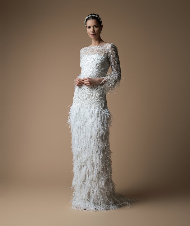 a model wears a wedding dress with intricate all over scallop detail hand beading and ostrich feather detail on the skirt.