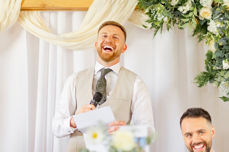 a best man laughs as he gives his speech.
