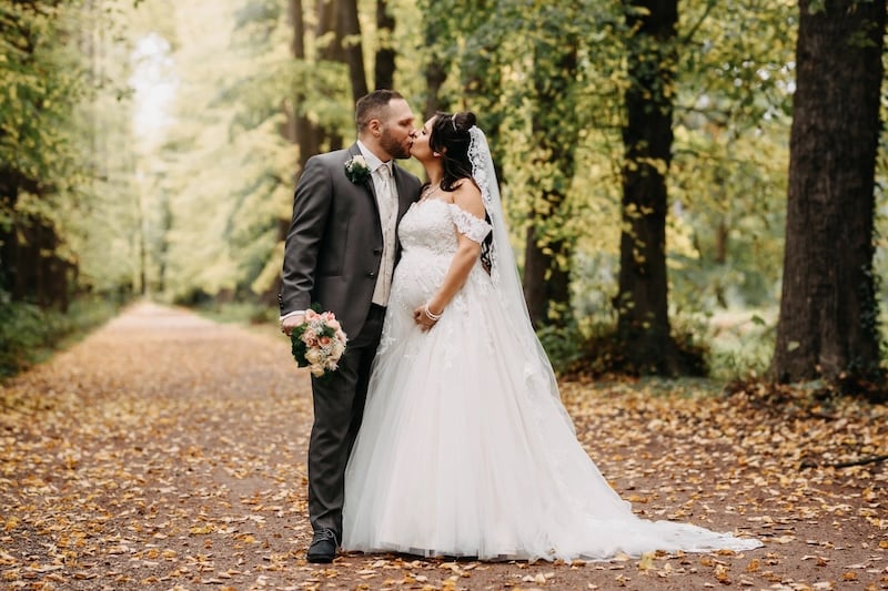 Hochzeitspaar küsst sich auf einer herbstlichen Allee
