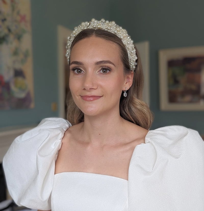 a bride wearing a puff sleeved wedding dress and beaded headband with natural wedding makeup smiles at the camera.