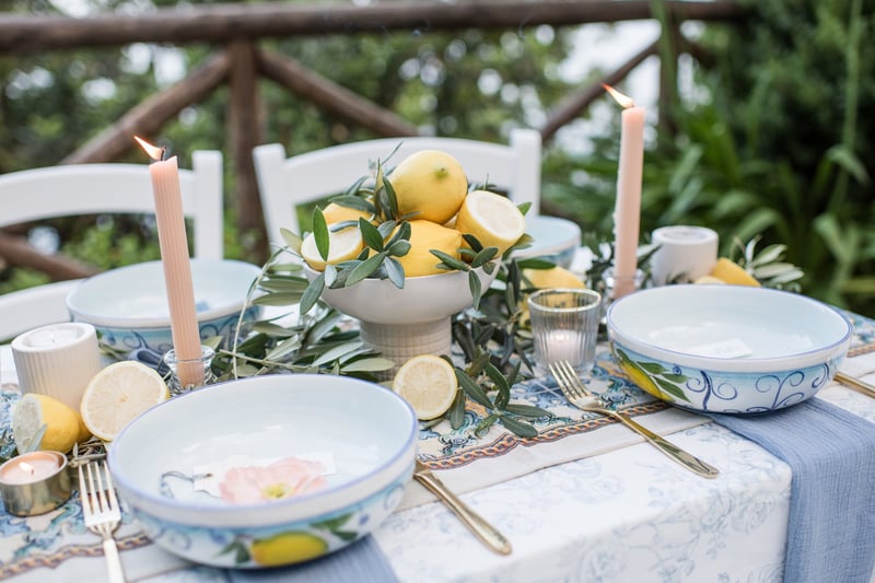 a summer wedding table set up with taper candles, porcelain bowls and citrus fruit and foliage tablecentres.