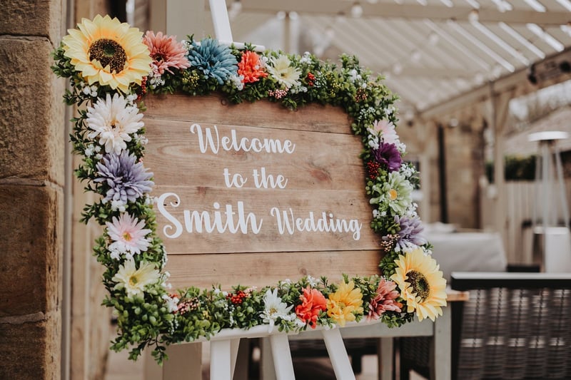 a rustic wooden wedding welcome sign with a bright floral border.