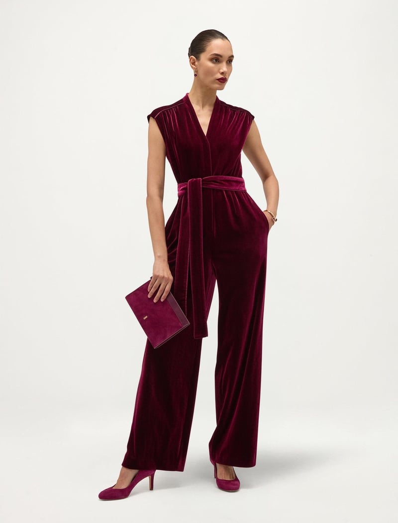 a model wears a plum-coloured velvet jumpsuit with matching shoes and clutch bag.