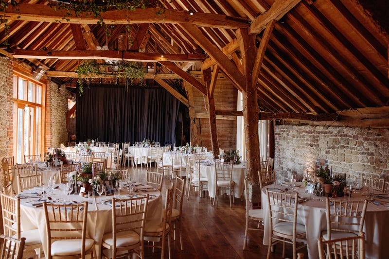 interior of a barn wedding venue set up for a wedding breakfast with round tables and white linen.