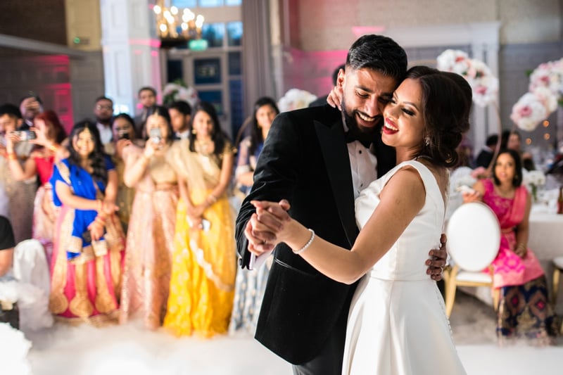 an Indian couple in western black tie attire enjoying their wedding first dance as guests look on 