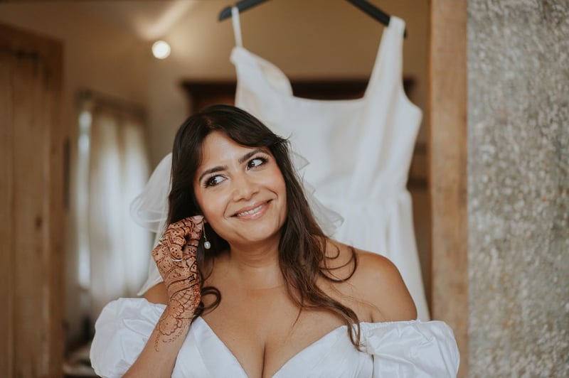 a bride with long dark hair smiles as she puts in her earrings.