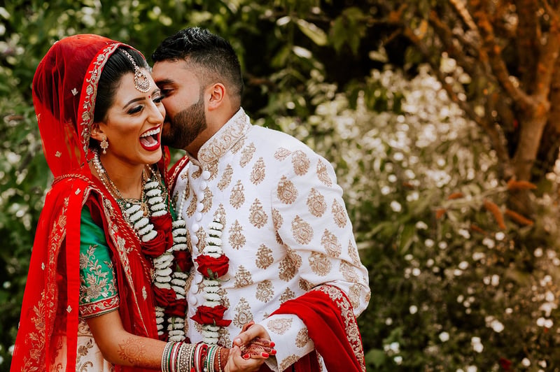 a Hindu bride and groom in traditional Indian wedding attire laughing as they embrace.