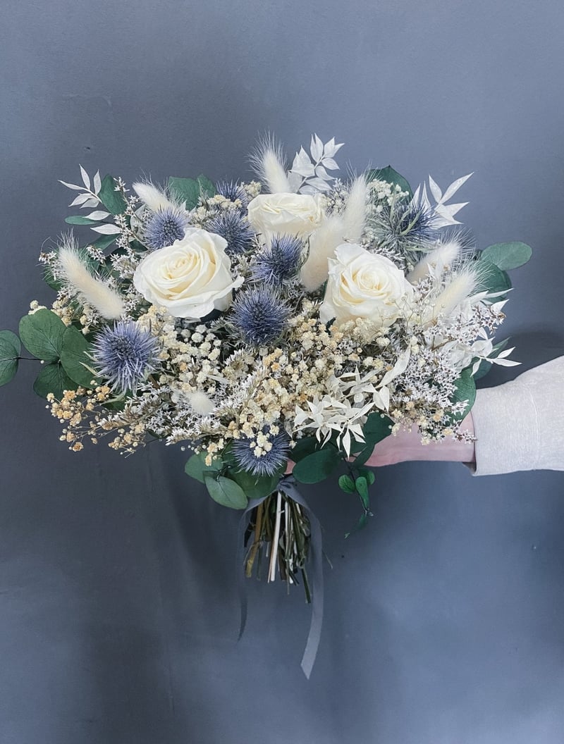 a hand holding a pale blue, white and green dried flower bouquet for a winter wedding.