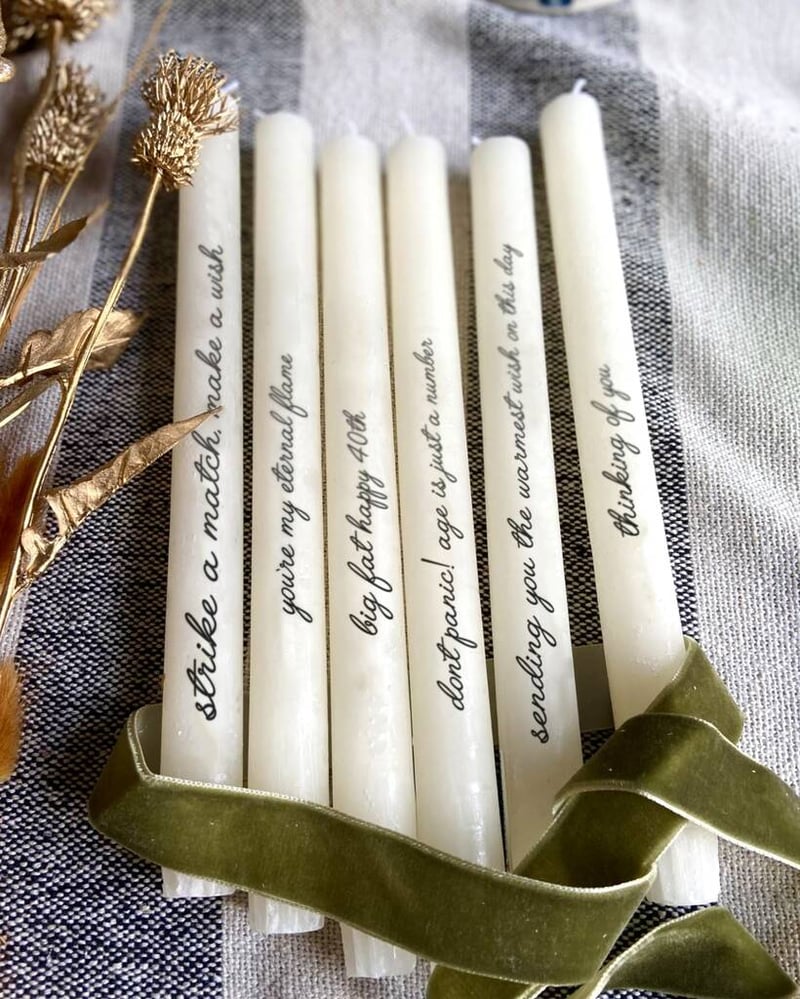 a collection of white tapered candles with personalised text on each one, tied with green velvet ribbon