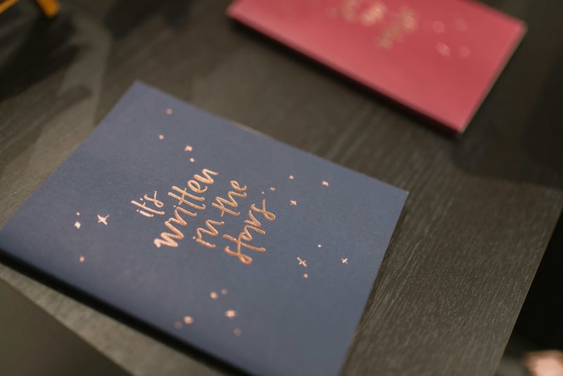 two wedding cards on a table, one reads 'it's written in the stars' in metallic font.