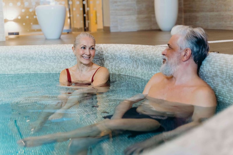 an older man and woman chatting as they sit inside a jacuzzi inside a spa.