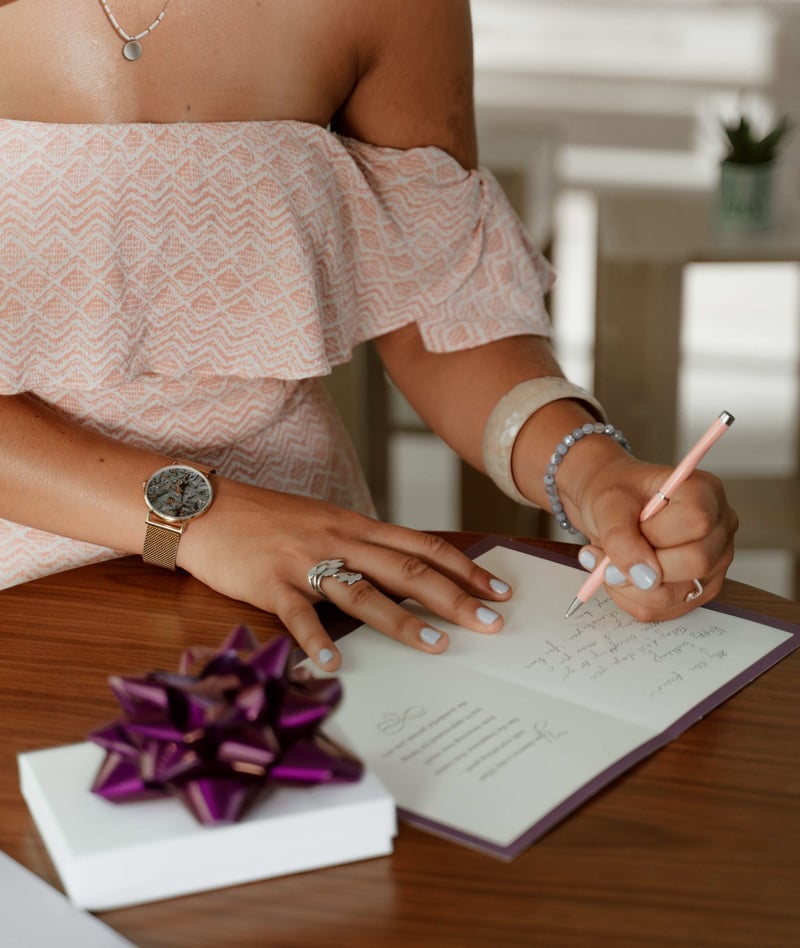 close up of a woman handwriting a wedding card. There is also a gift on the table.