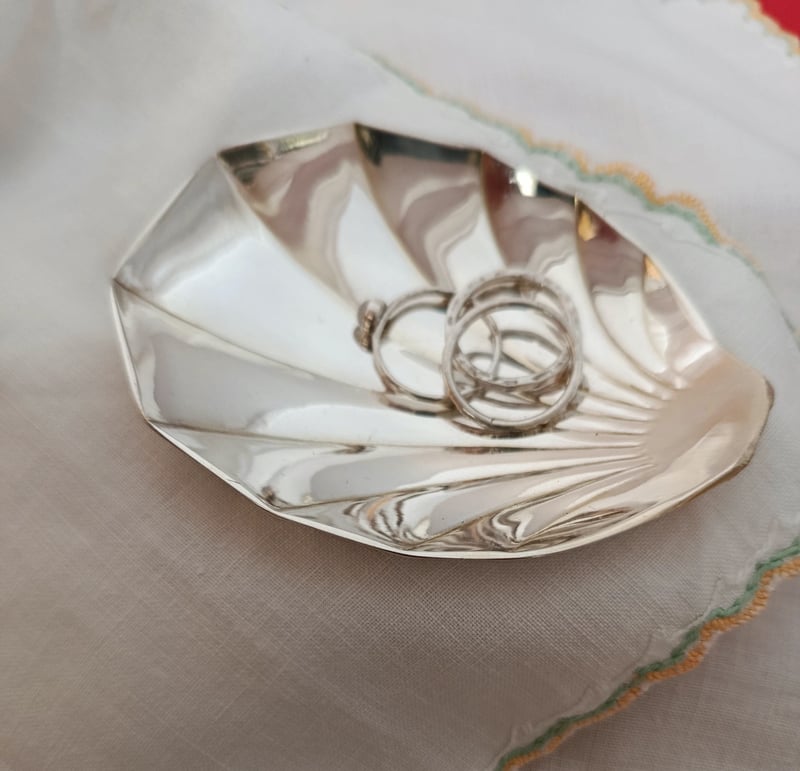 a silver trinket dish shaped like a scallop shell holding a pair of white gold rings.