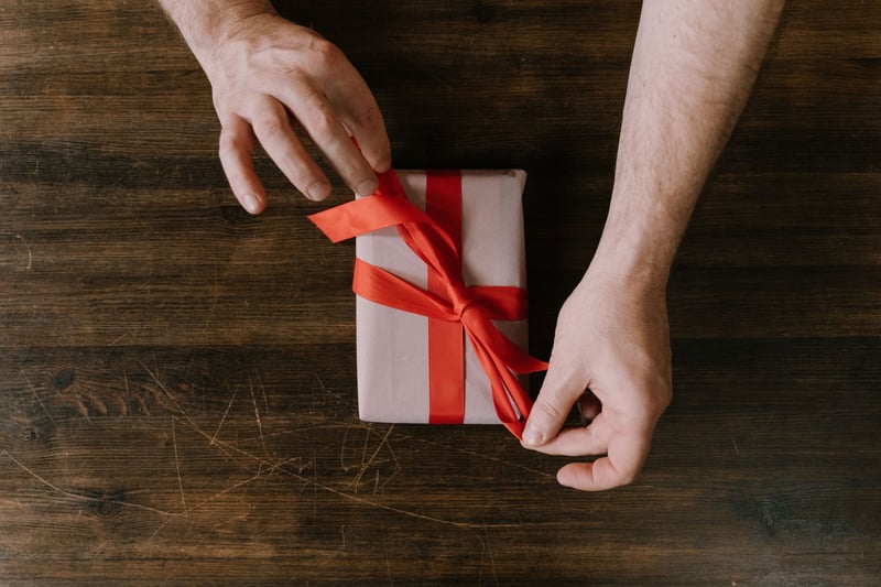a pair of hands tying red ribbon on a present.