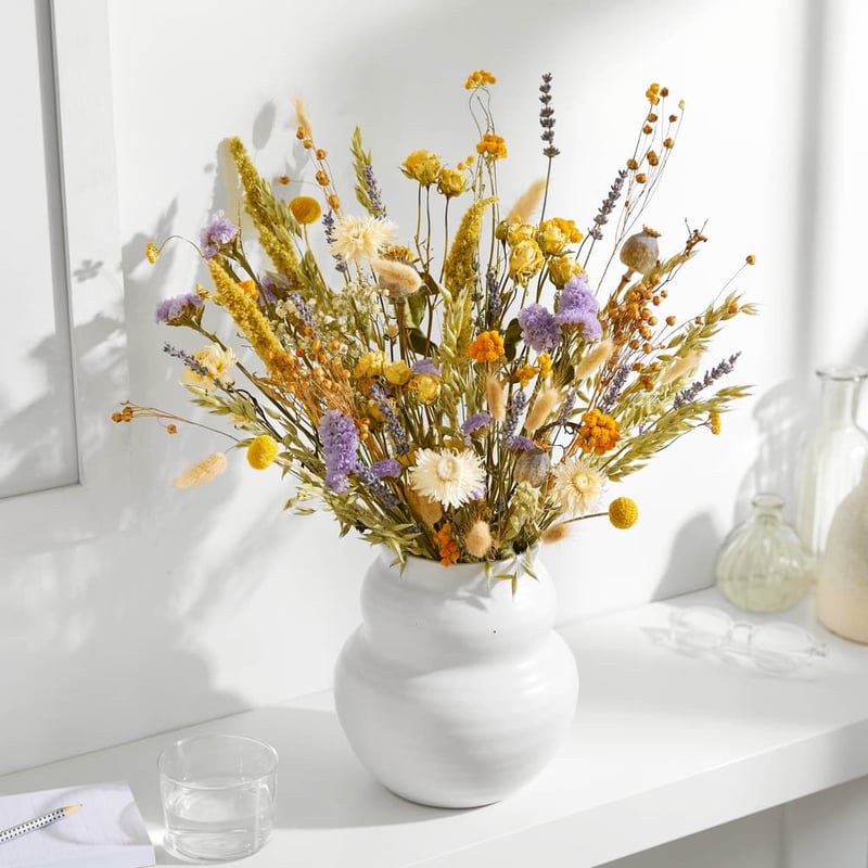 a white vase with a dried flower bouquet in oranges, yellows and purples.