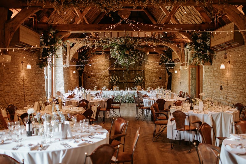 interior of a winter wedding barn set up for a wedding breakfast with round tables, fairylights and lots of winter foliage.