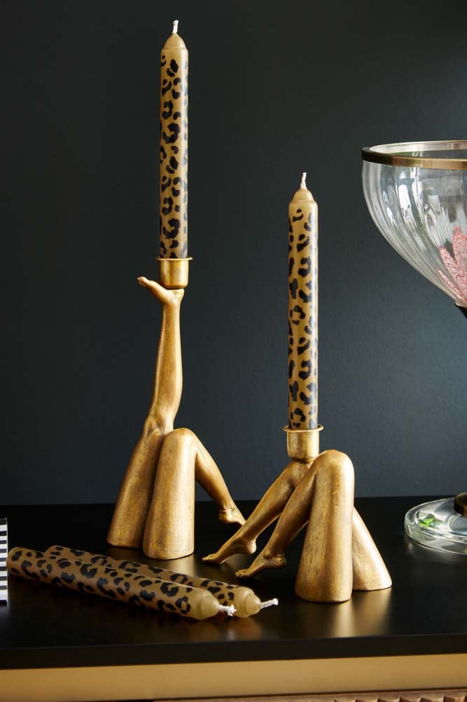 a set of four leopard print taper candles, two of which are inside a holder resembling women's legs