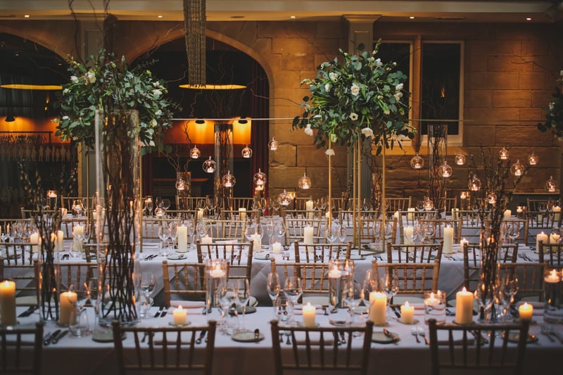 interior of a conservatory in a country manor house with candlelit long tables and tall green and white floral tablecentres.