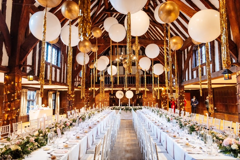interior of a barn venue set up for a winter wedding with long tables and giant balloons hanging from the beams.