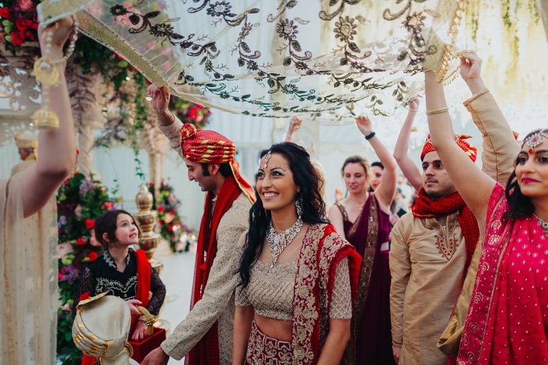 a Hindu bride and groom underneath a canopy at their ceremony as guests stand behind.