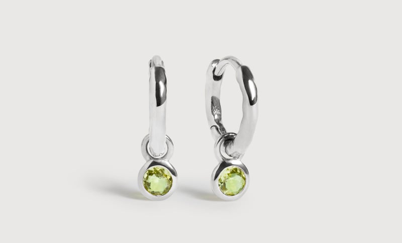 a pair of sterling silver huggie hoop earrings with single green peridot gemstones.