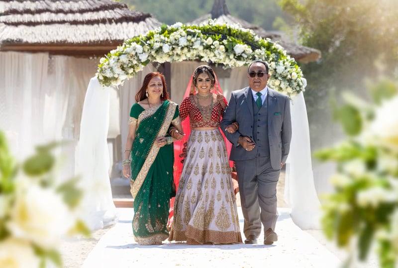 an Indian bride walks down the aisle arm in arm with her parents.