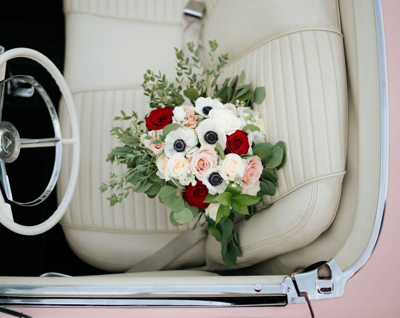 a winter wedding bouquet include white and black anemones on the seat of an open top car.