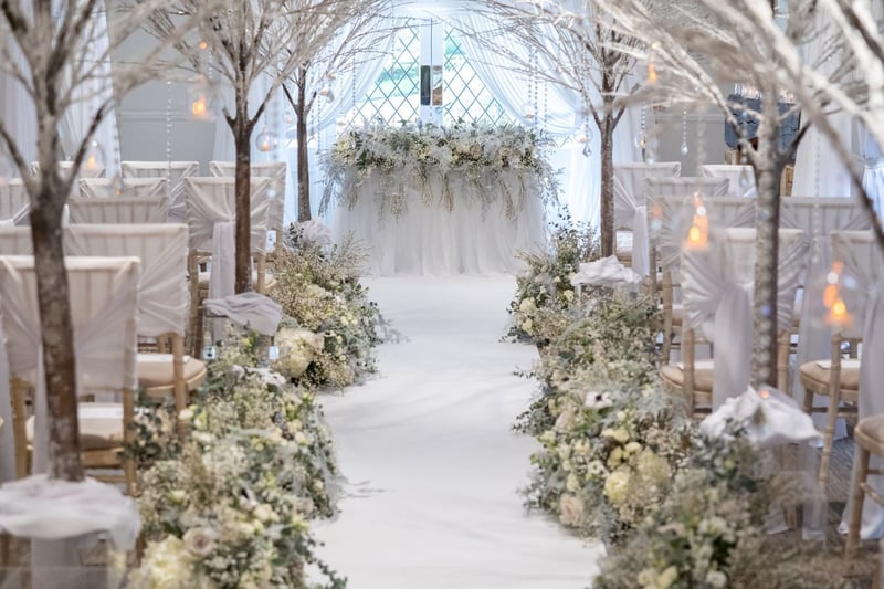 a winter wedding ceremony set up with icy details like frozen trees and white floral arrangements on the ceremony table, aisle and chair ends.